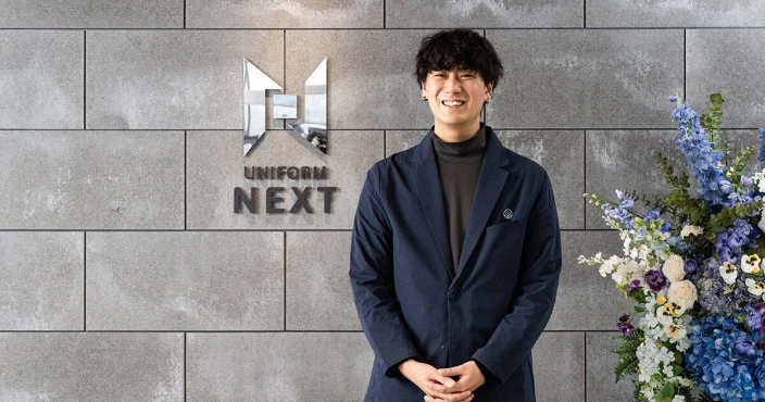 ユニフォームネクスト株式会社様のロゴと、社員の方を写した写真。